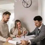 Un couple discute d'un plan avec un agent immobilier, planifiant l'achat de leur nouvelle maison.