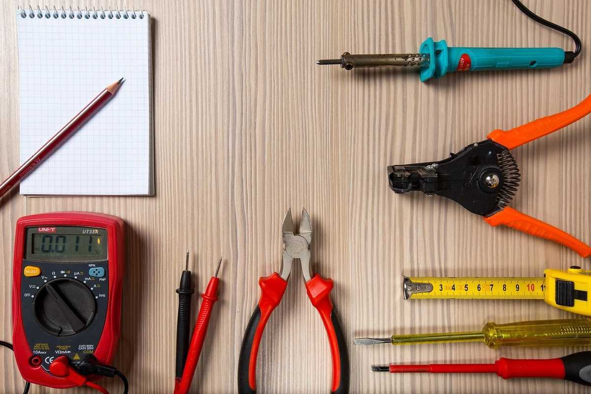 Outils de bricolage sur une table en bois, incluant un mètre, des pinces, un multimètre, et un carnet avec un crayon Outils de bricolage sur une table en bois, incluant un mètre, des pinces, un multimètre, et un carnet avec un crayon