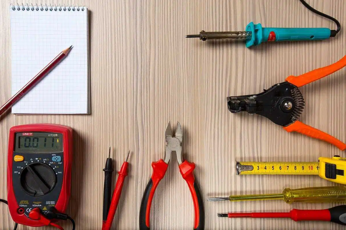 Outils de bricolage sur une table en bois, incluant un mètre, des pinces, un multimètre, et un carnet avec un crayon Outils de bricolage sur une table en bois, incluant un mètre, des pinces, un multimètre, et un carnet avec un crayon