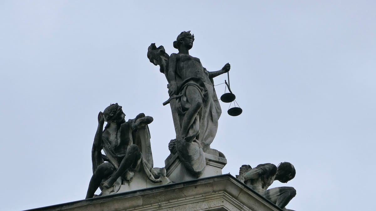 Statue de la Justice tenant une balance, avec figures allégoriques et ciel bleu